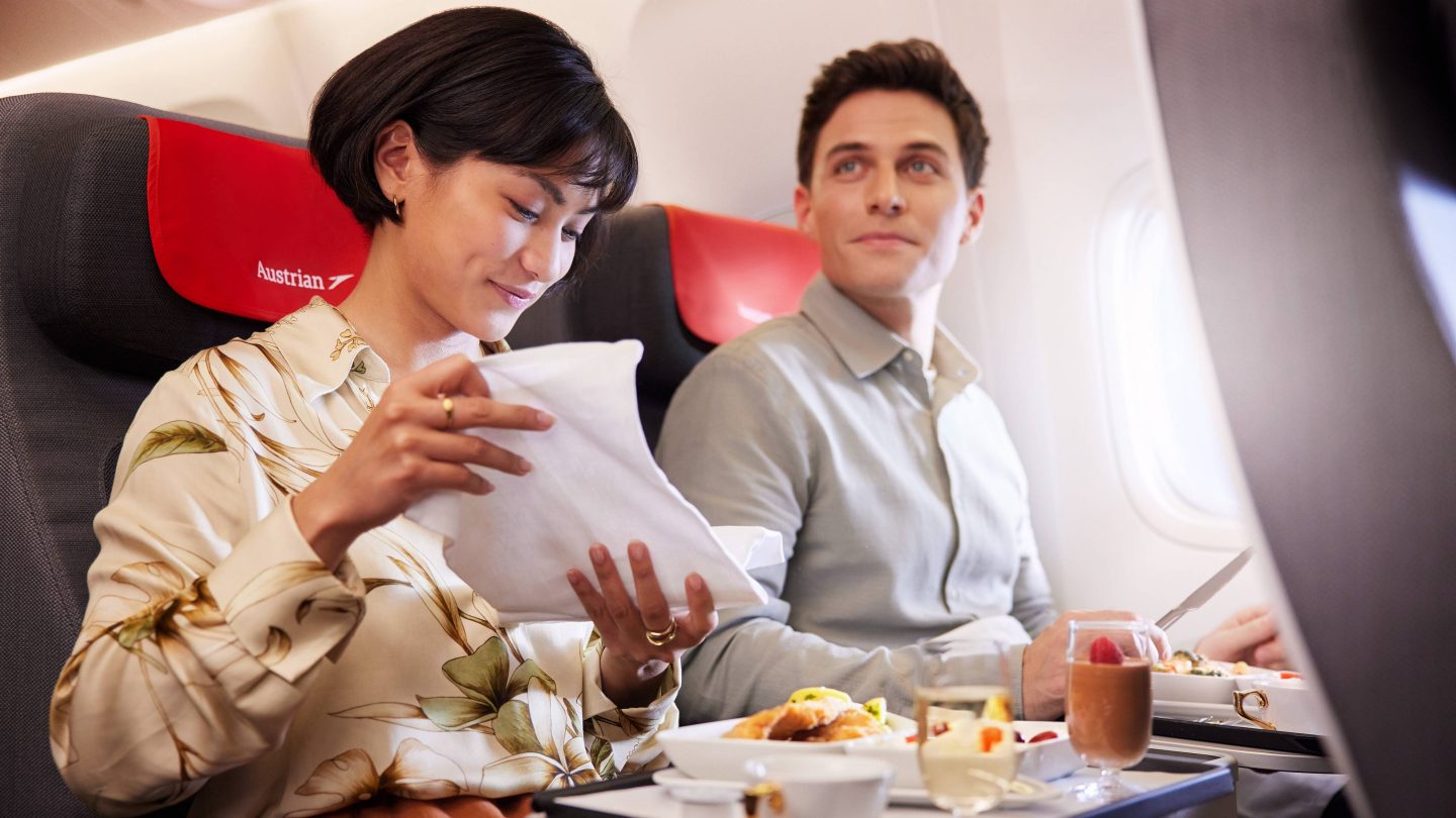 A man and woman dining on an airplane, with trays of food in front of them as they travel.