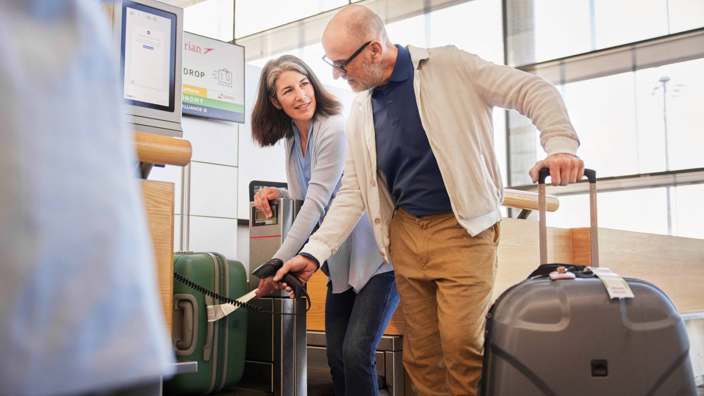 A man and woman scan a luggage tag at an airport self-service kiosk.