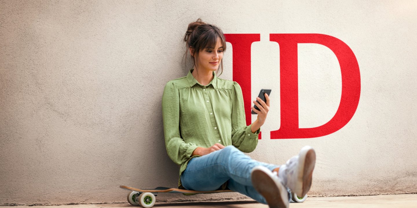 Young woman sitting on skateboard, using smartphone