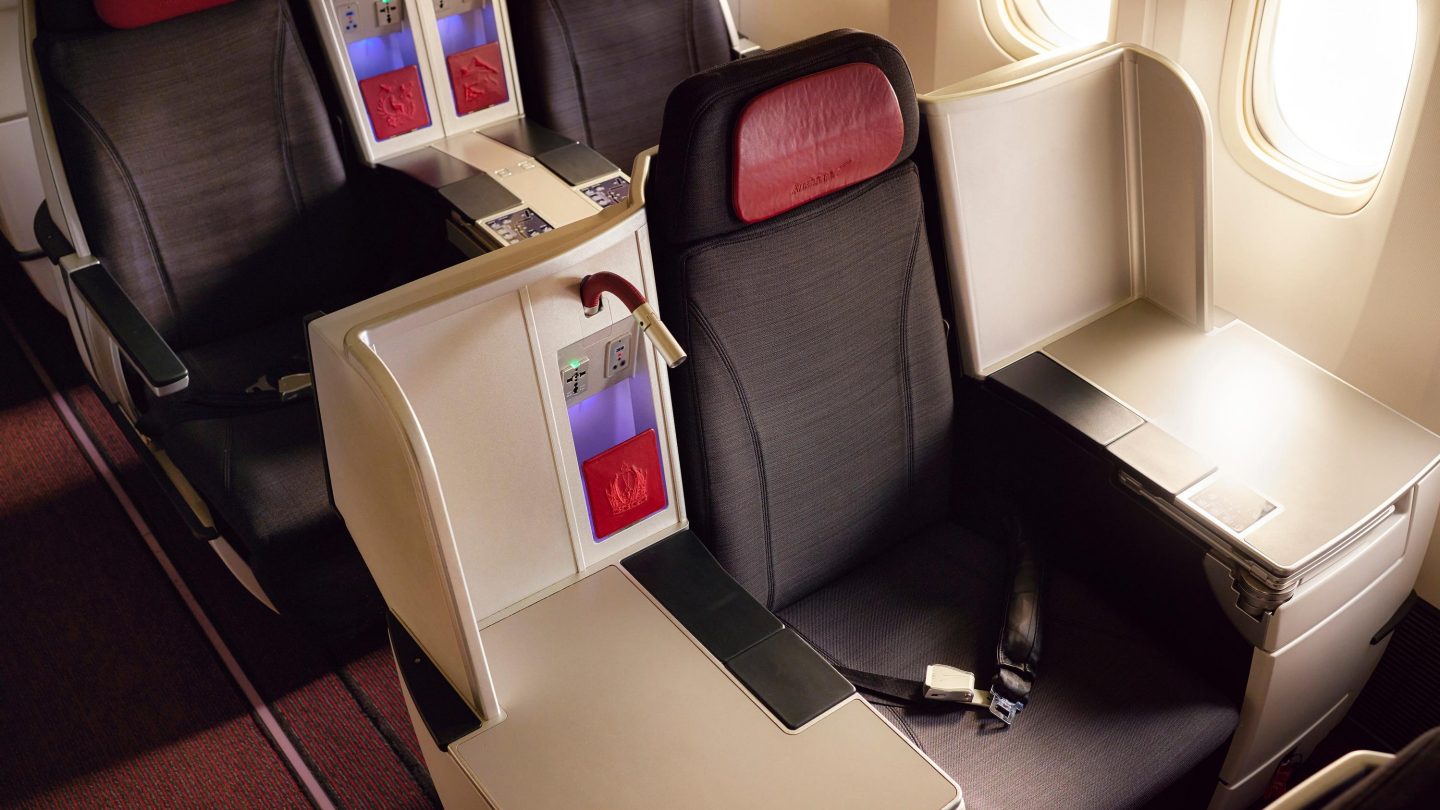 Asientos de Business Class con tapicería roja y negra, separados por una consola con almacenamiento y tomas de corriente.