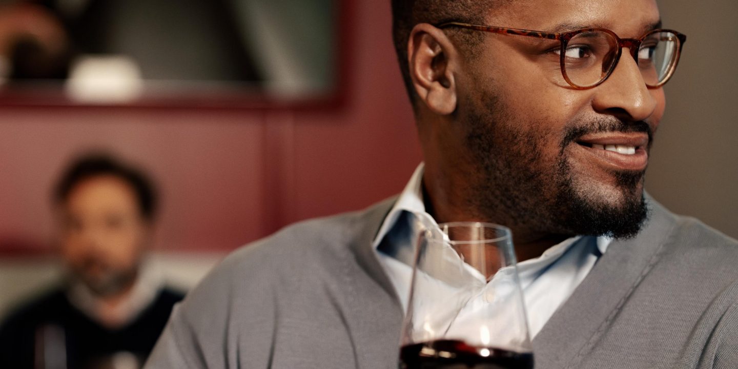 Smiling man holding a glass of red wine in a lounge.