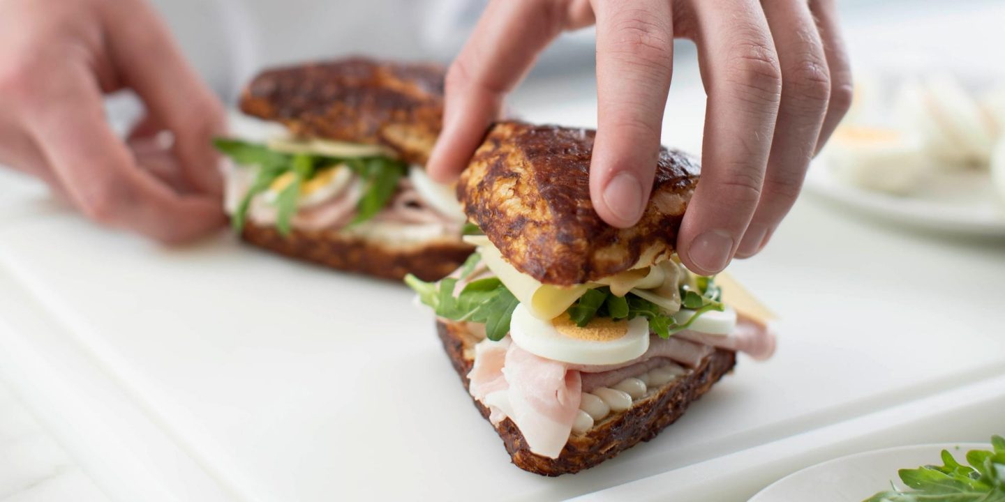 Hands assembling a fresh ham and egg sandwich
