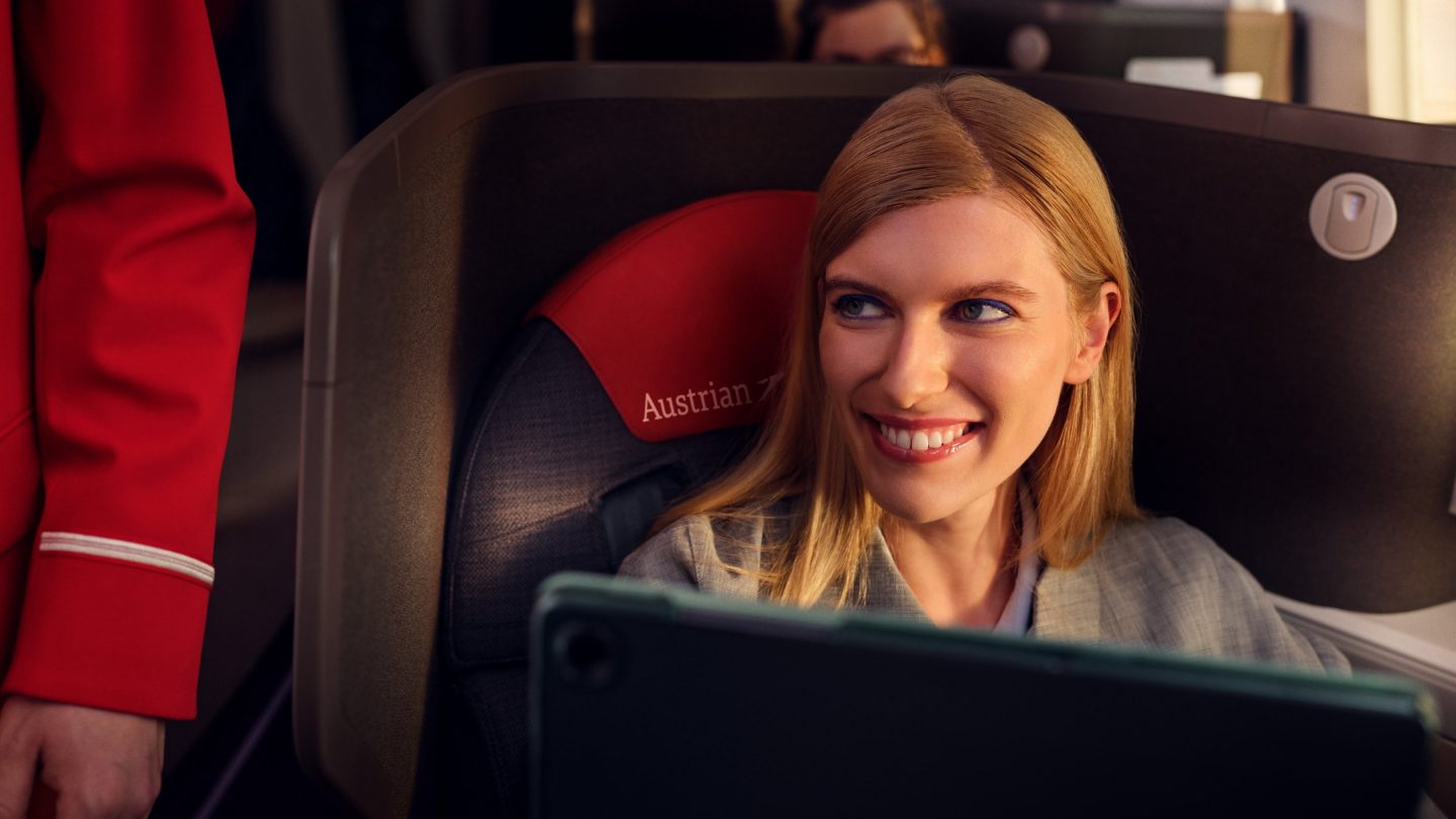 オーストリア航空の席に座り、タブレットを見つめる笑顔の金髪の女性。