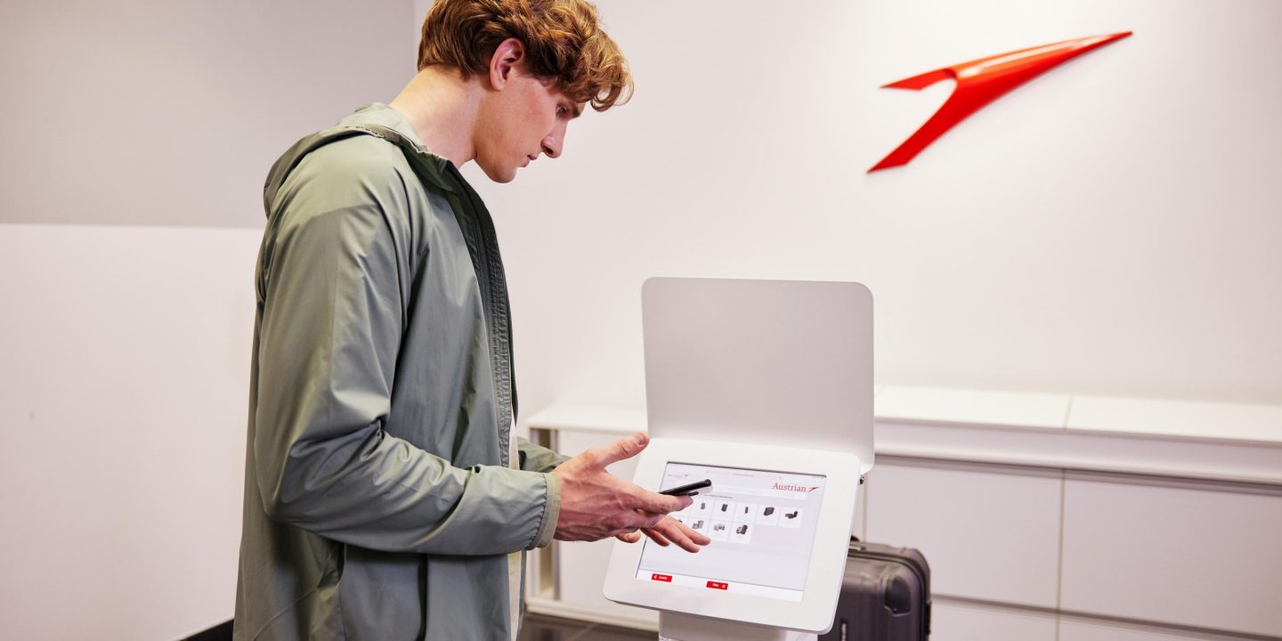 Passenger using Austrian Airlines self-service bag drop kiosk.