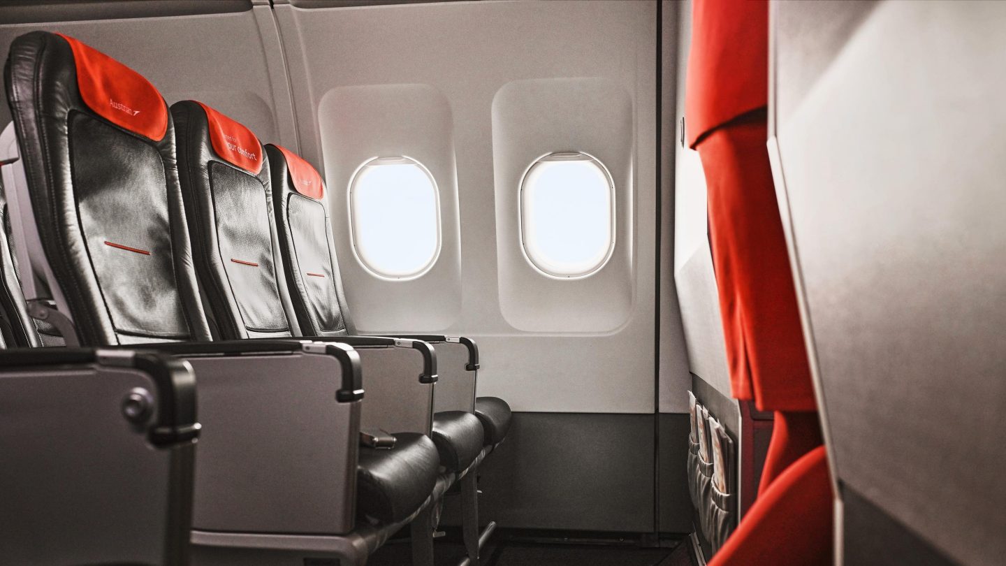 Kabine von Austrian Airlines: dunkle Sitze, orangefarbene Kopfstützen und helle Fenster.