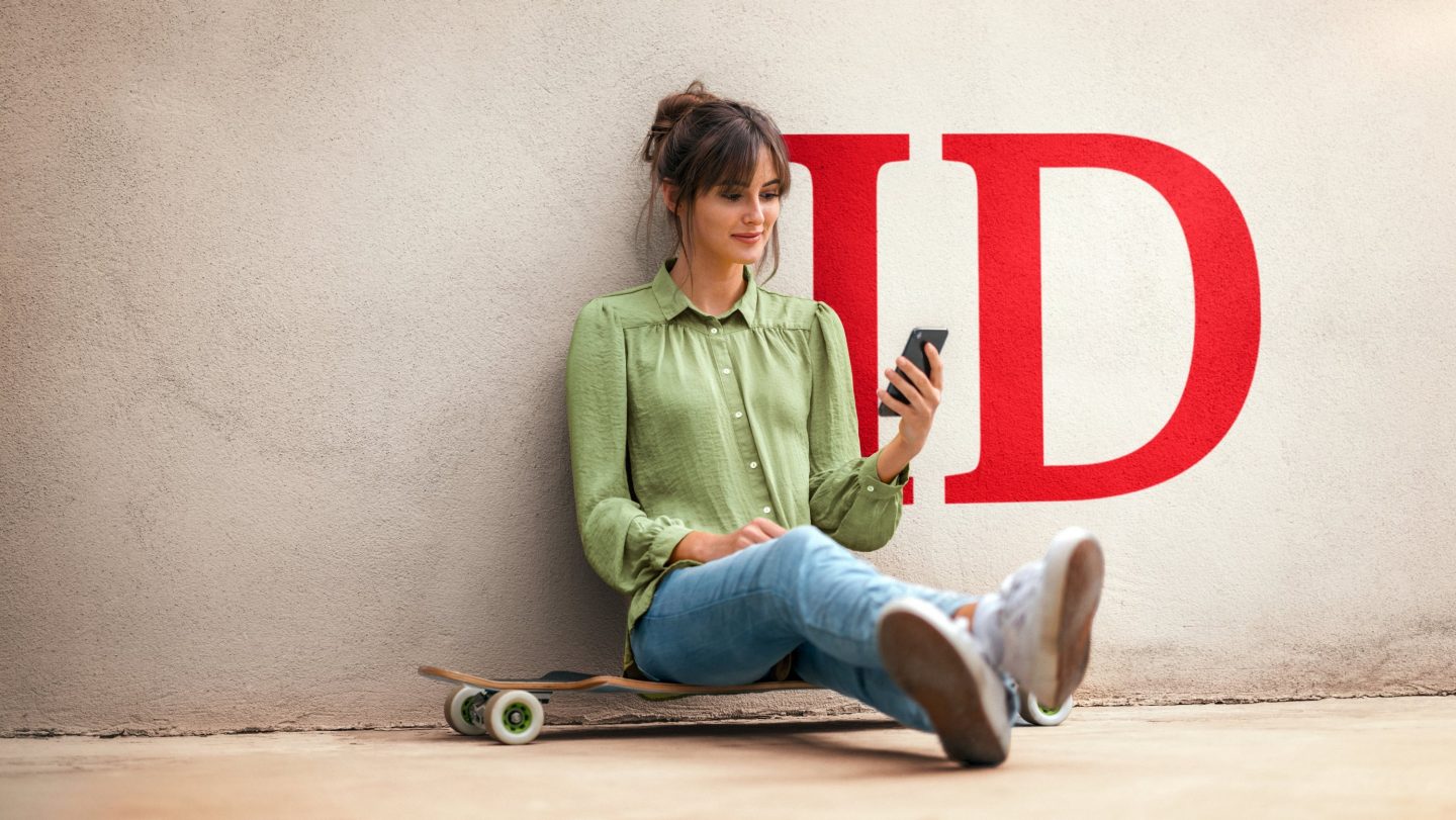 Kobieta na deskorolce patrząca na swój smartfon na tle czerwonego logo „ID”.