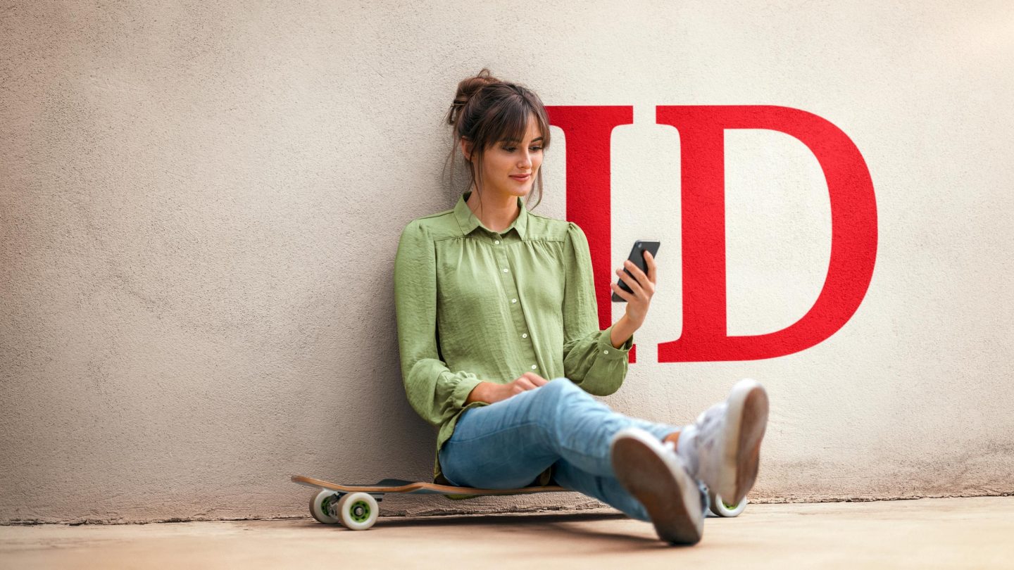 Young woman sitting on skateboard, using smartphone