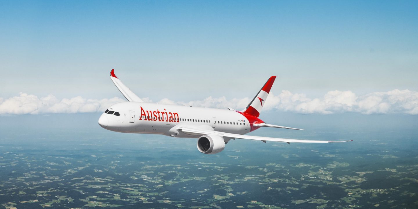 Ein Boeing 787 Dreamliner der Austrian Airlines im Flug über grünen Landschaften.