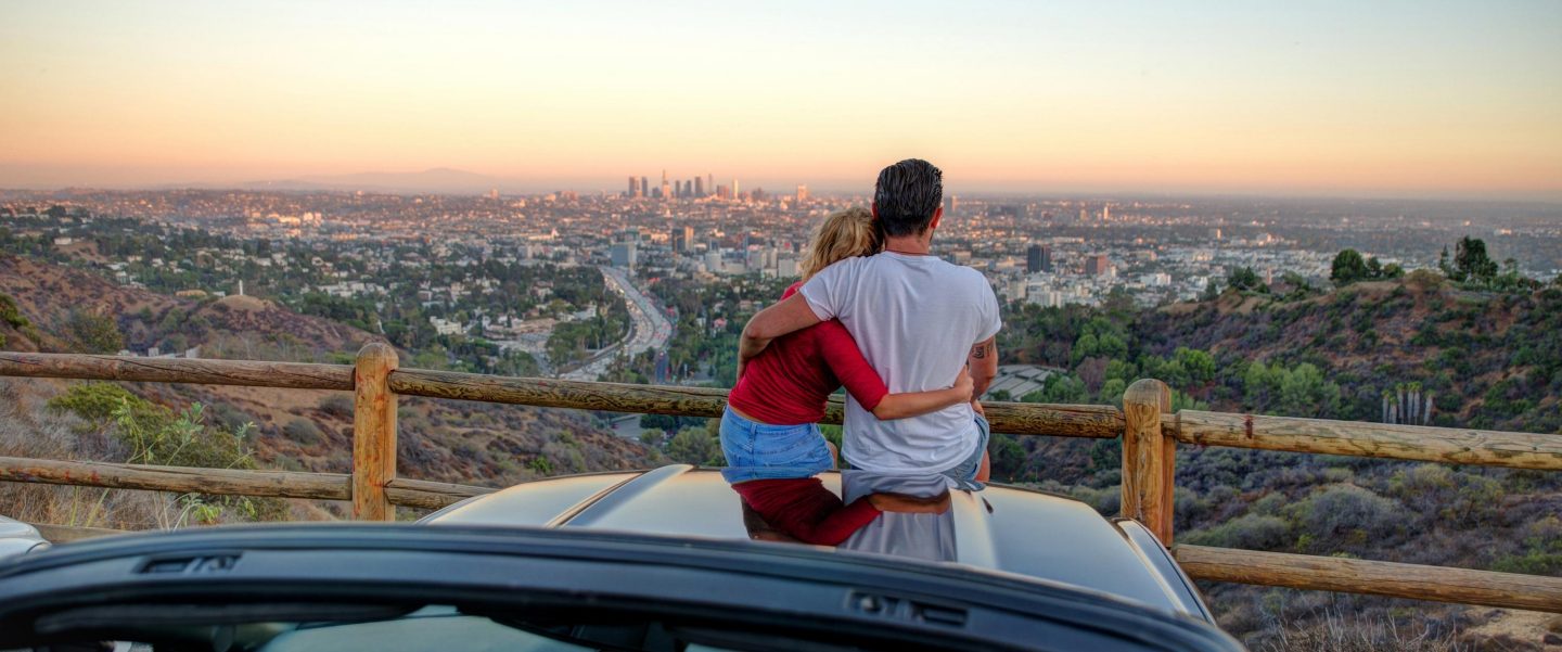 Couple watching sunset from popular view point in Los Angeles, California. Sitting on the sport convertible car hood