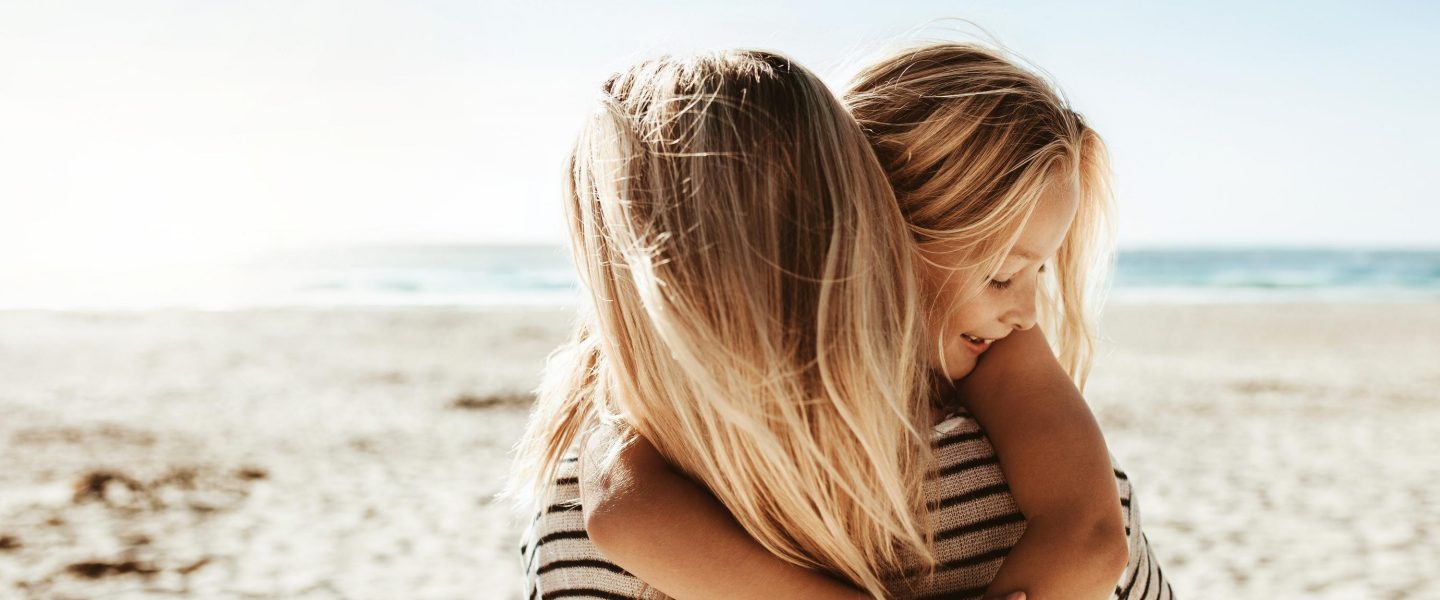 Rear view of a woman carrying her daughter and walking along the beach. Family on a summer beach vacation.