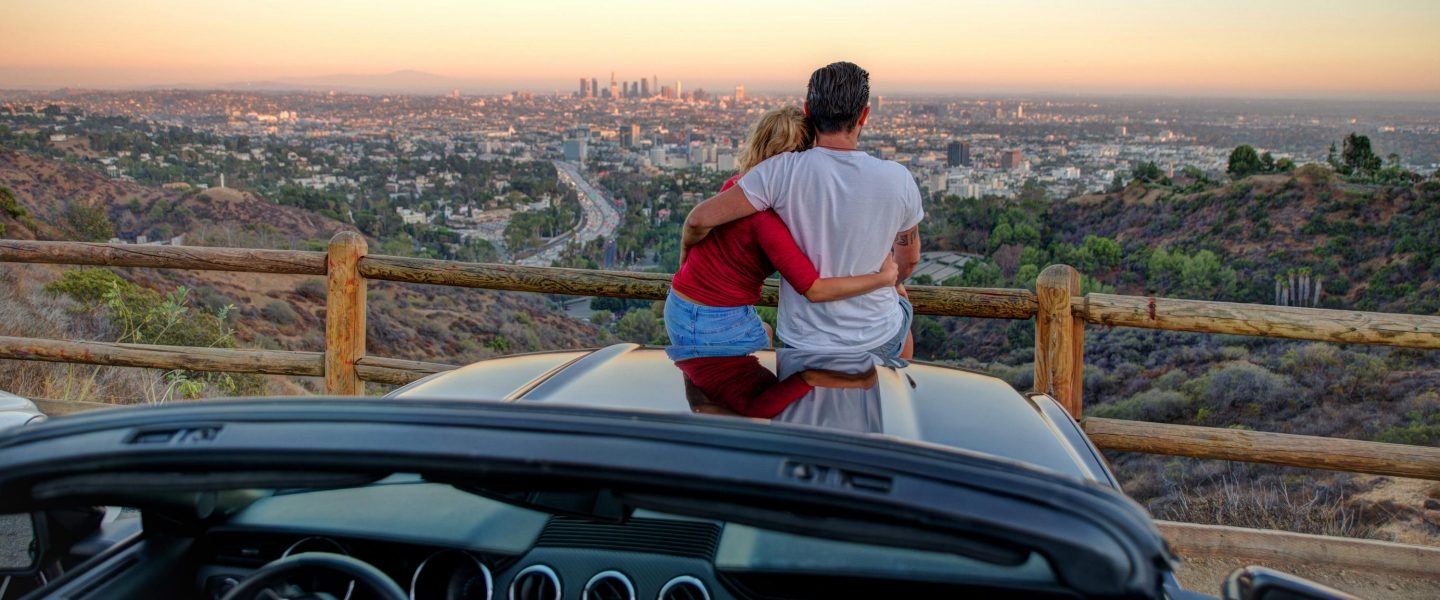 Couple watching sunset from popular view point in Los Angeles, California. Sitting on the sport convertible car hood