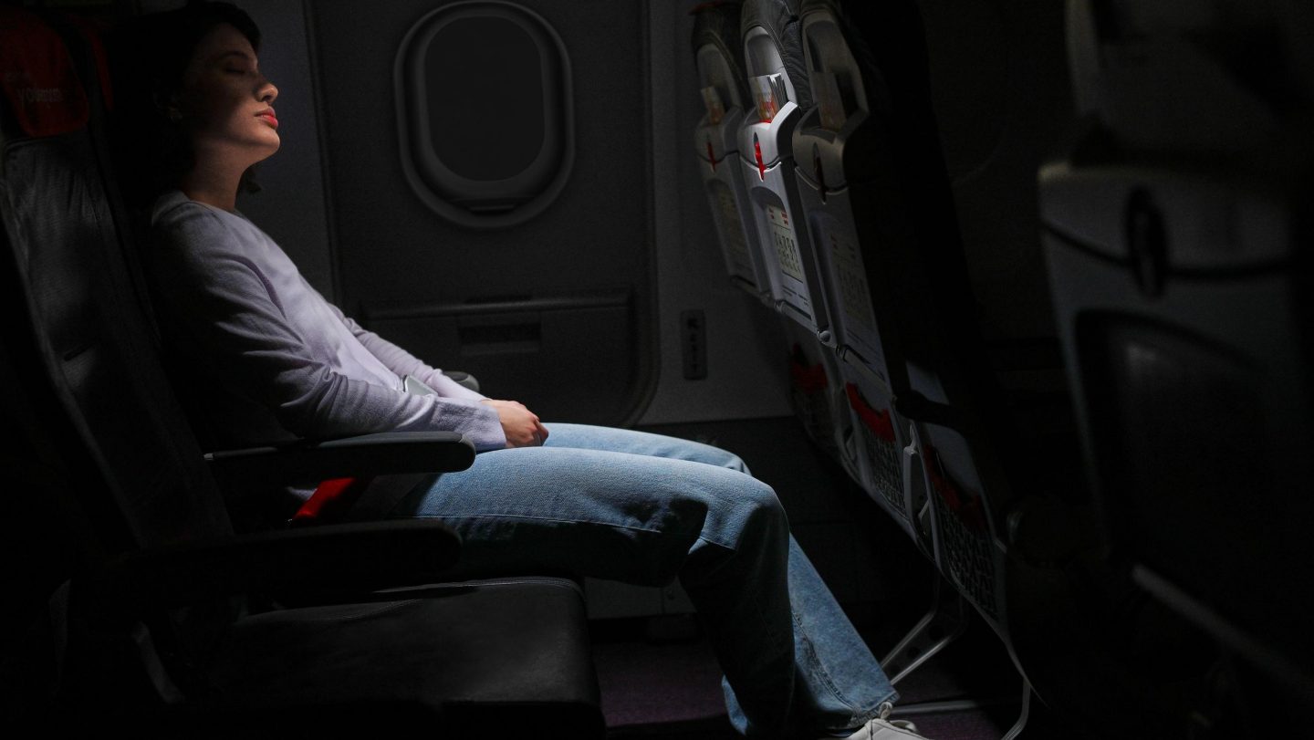 Una persona, que parece tranquila y relajada, recostada en un asiento de avión con iluminación tenue.