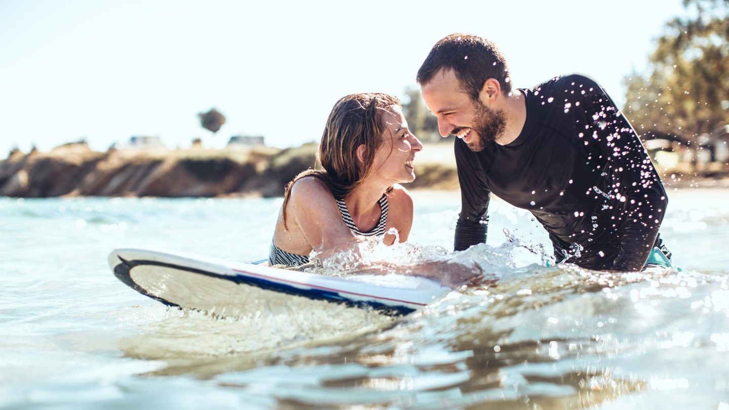 Loving couple of smiling surfers in the water, flirting while waiting for a good wave to come