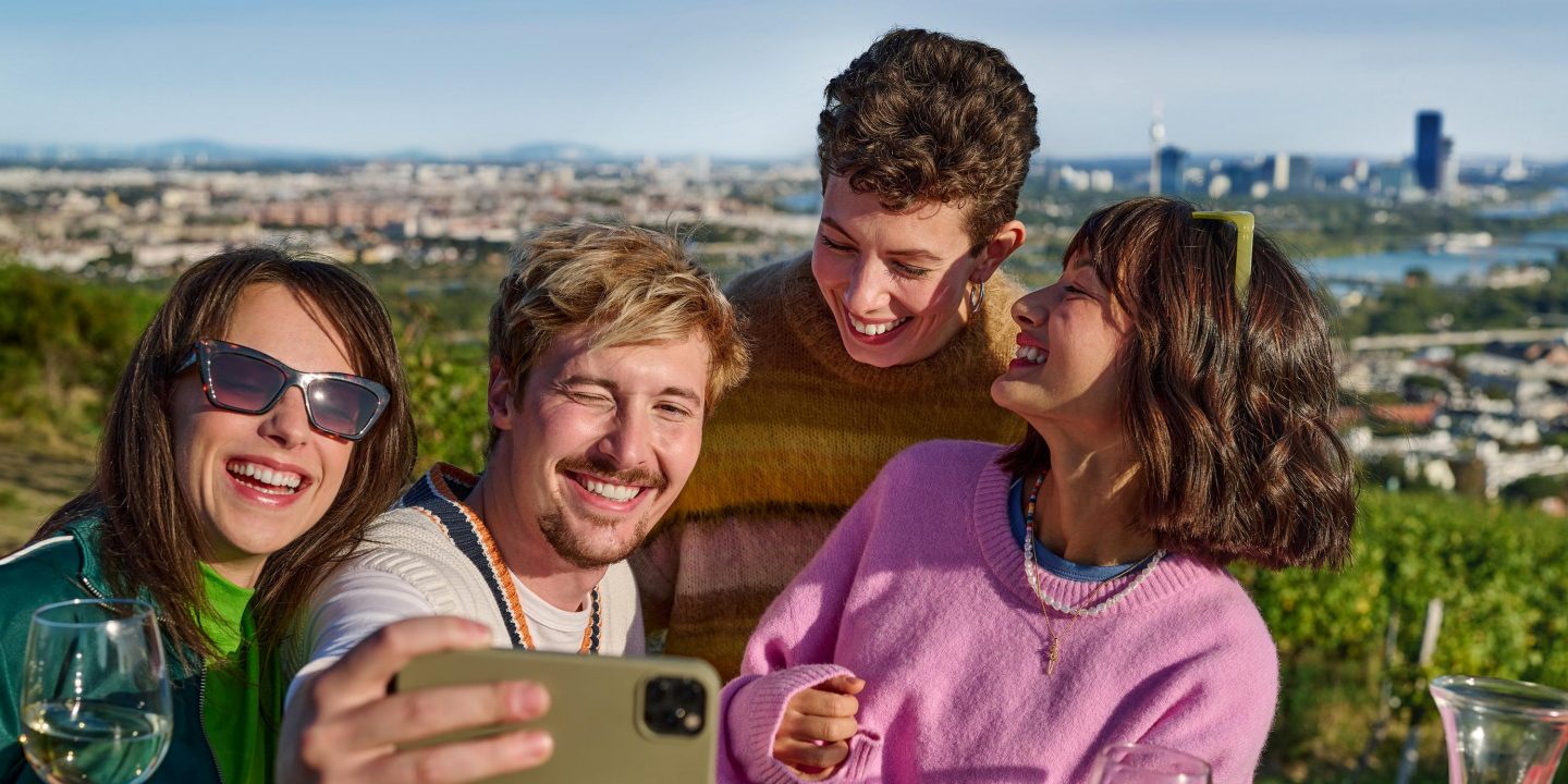 Four friends smiling and taking a selfie outdoors.