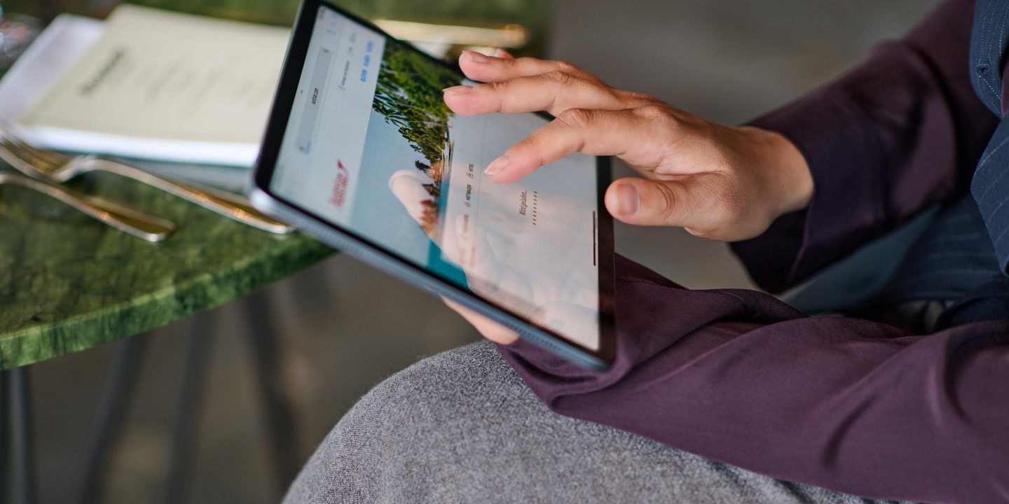 Hands using a tablet to browse a travel website.