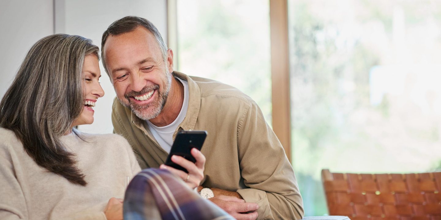 Happy couple laughing looking at a phone, planning their next journey.