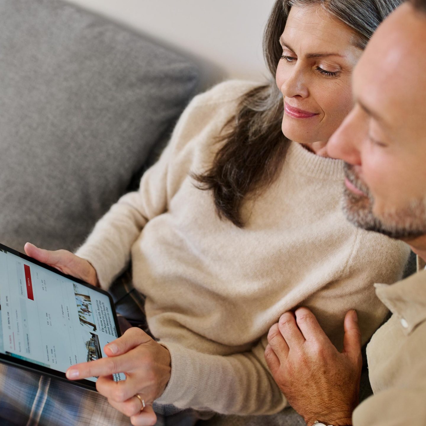 Ein lächelndes Paar sitzt zusammen zu Hause und schaut auf ein Tablet.