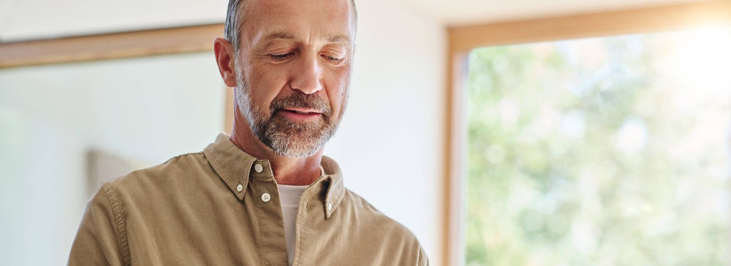 A mature man smiling, wearing a beige button-down shirt.