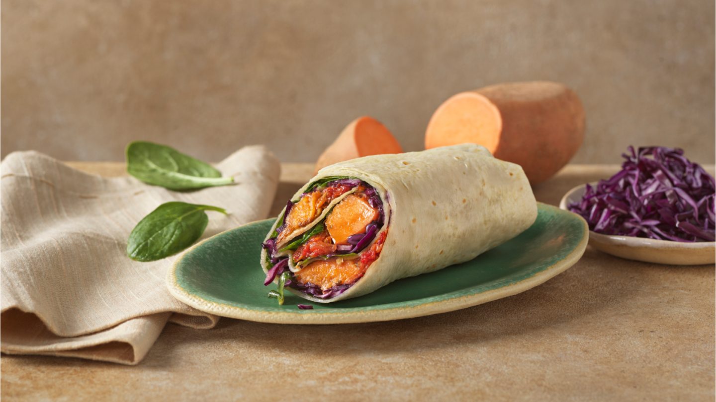 A vegetarian wrap with sweet potato, red cabbage, and spinach on a green plate.