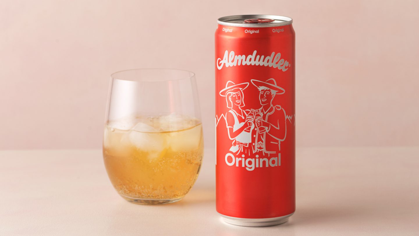Almdudler can and glass with ice on a peach surface.