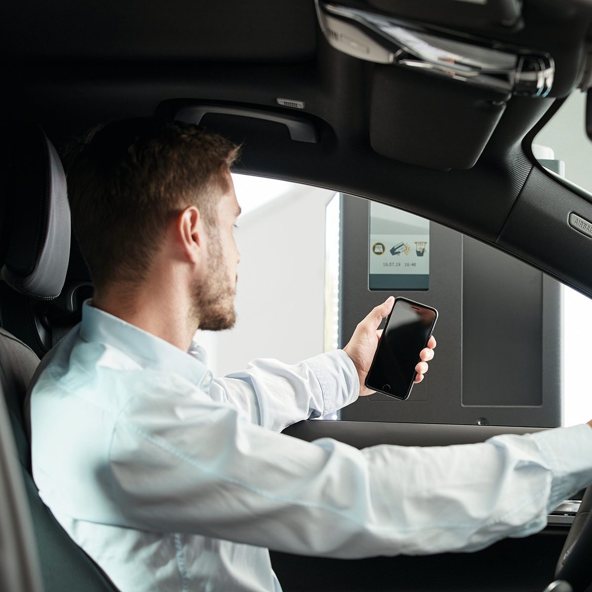 A man in a car scanning his smartphone at a parking terminal.