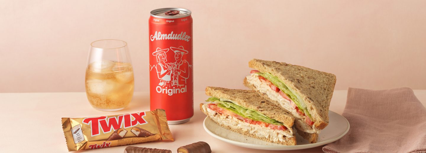 Inflight meal combo: sandwich, Almdudler drink with ice, and a Twix bar.