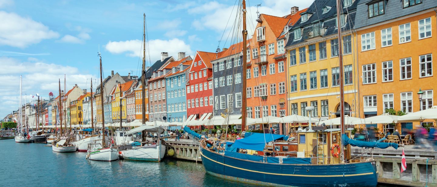 Colorful waterfront buildings along Nyhavn Canal in Copenhagen, with boats moored by the promenade.