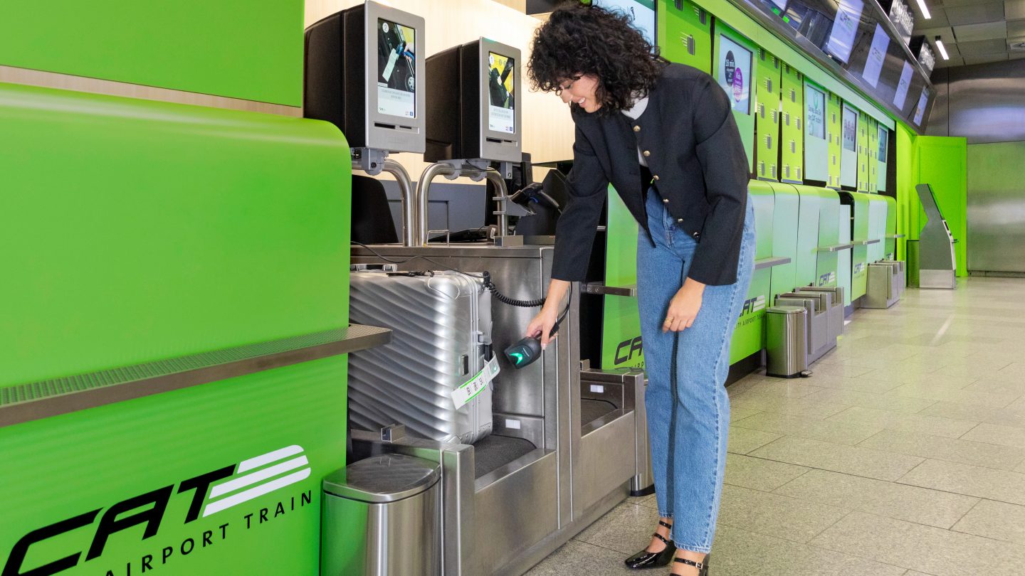 Person scannt Gepäck am Self-Check-in-Kiosk mit CAT-Airport-Branding.