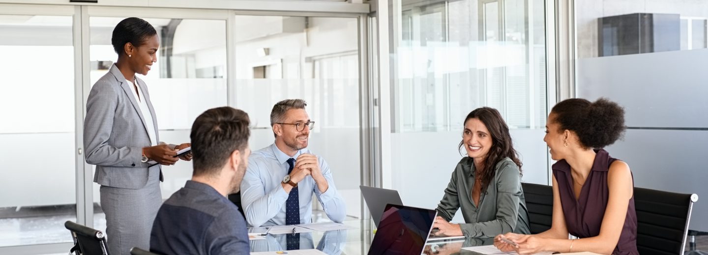 Smiling business team discussing work in meeting using laptop and documents in conference room. Successful business woman and businessmen discussing marketing strategy and ideas at meeting room. Corporate business man and woman with manager and secretary working together.