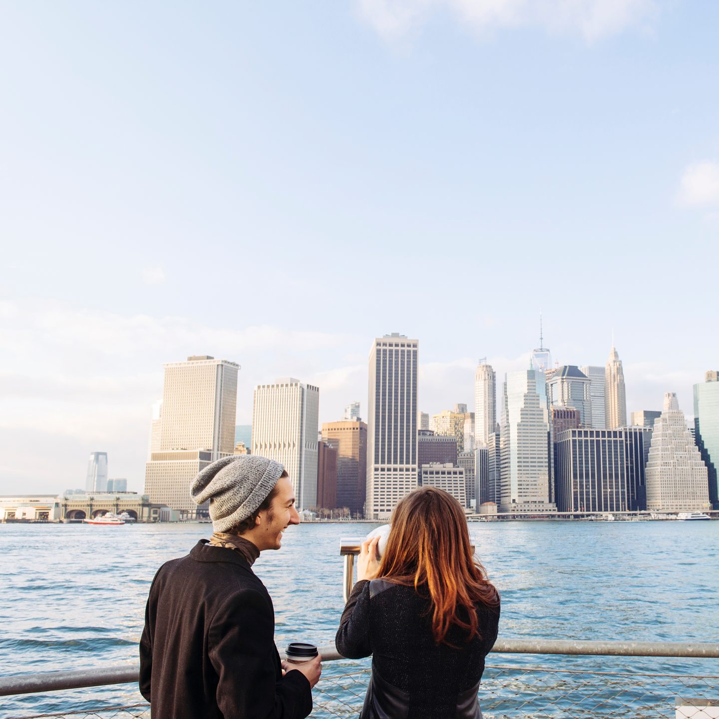 A man and a woman sitting by the water, looking at the New York City skyline.
