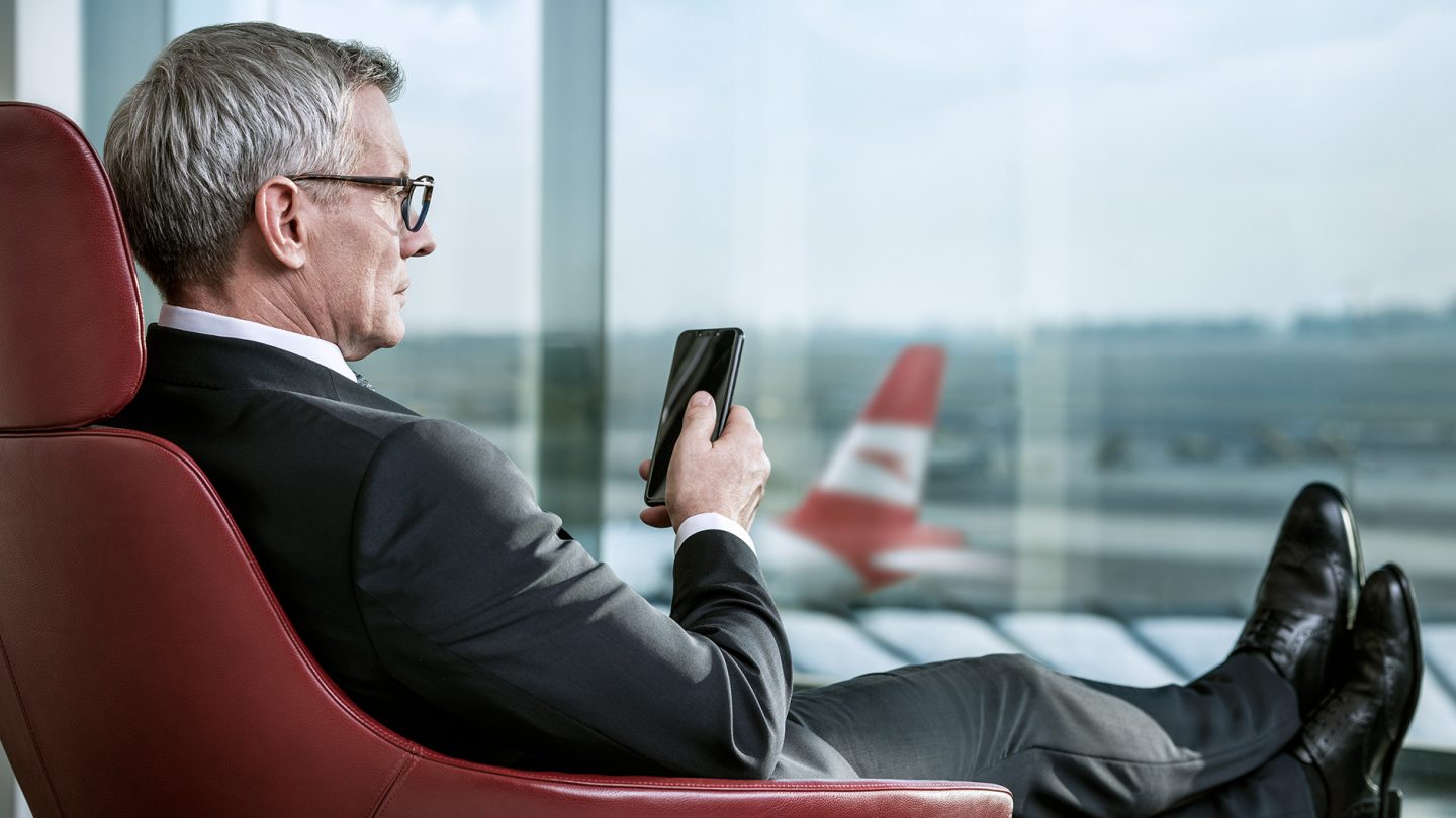 A business traveler sits at the gate and looks at his smartphone
