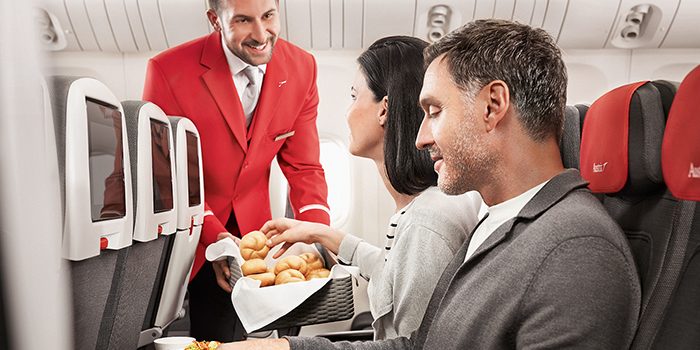 An Austrian flight attendant hands bread rolls to a passenger