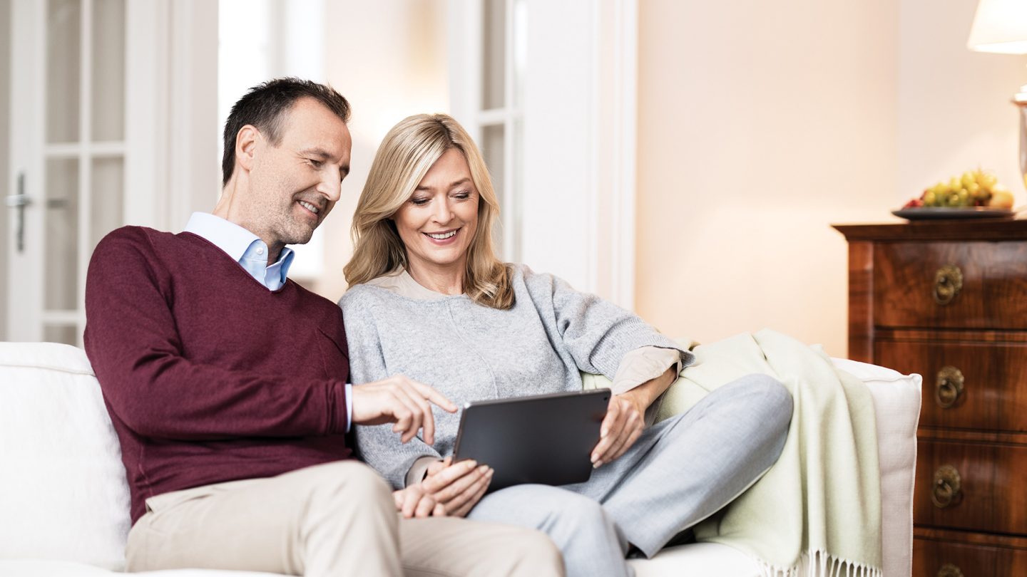 A couple is sitting on the sofa with a tablet